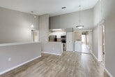 Located at 11000 Point Sylvan Circle in Orlando, FL, this 2-bedroom, 2-bathroom home offers a well-designed single-level layout with modern finishes throughout. The open-concept living, dining, and kitchen area forms the heart of the home, featuring soaring vaulted ceilings with pendant lighting, light wood-look flooring, and a neutral warm-gray color palette that creates a bright and cohesive atmosphere. A half-wall with a breakfast bar separates the kitchen, which is equipped with stainless steel appliances including a refrigerator, range, and microwave, complemented by white cabinetry and granite-style countertops. A convenient in-unit laundry area is tucked just off the kitchen. The primary bedroom is a standout feature, boasting a vaulted ceiling, an arched window that floods the room with natural light, views of lush greenery, a ceiling fan, and a spacious walk-in closet with wire shelving. The second bedroom is also well-proportioned with a ceiling fan and a window overlooking the outdoors. Both bathrooms offer consistent finishes with white vanities, tub-shower combinations, and wood-look tile flooring. Additional storage is provided by multiple closets, and a den adds flexible living space. The home also includes a staircase, suggesting access to an entry or utility area below.