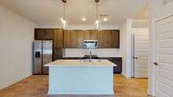This single-story residence showcases a thoughtfully designed open-concept layout with consistent wood-look flooring connecting the main living areas. The kitchen serves as the focal point of the space, featuring rich, dark-toned cabinetry extending to the ceiling for ample storage, paired with crisp white quartz countertops that provide strong visual contrast. A generously sized central island includes an integrated sink and is illuminated by two pendant lights with elegant glass housings in a brass finish, making it ideal for both meal preparation and casual dining. The white subway tile backsplash adds a clean, classic element to the kitchen design, while stainless steel appliances — including a refrigerator with water dispenser, range, and over-the-range microwave — complete the functional setup.

The living area is bright and open, with natural light entering through front-facing windows, complemented by a ceiling fan overhead. The entryway is welcoming, featuring a paneled front door with a transom window above. A full bathroom includes a tiled tub-shower combination, dark vanity cabinetry with light countertops, and wood-look tile flooring. Additional rooms offer neutral walls, ceiling fans, and wood-look flooring, providing versatile, move-in-ready spaces throughout.