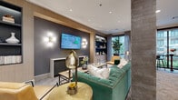 This thoughtfully designed amenity lounge offers a sophisticated social environment across a single floor, combining multiple distinct activity zones within one open, cohesive layout. The space transitions seamlessly from an elegantly appointed lounge area to an entertainment-focused game room and flexible gathering spaces.

The lounge area anchors one end of the space, featuring a tufted green velvet sofa with brass nail-head trim, a wall-mounted television set against a textured dark accent wall, and built-in shelving framed by warm wood paneling. Decorative globe wall sconces and a polished gold table lamp add warm, layered lighting throughout.

A sleek bar counter with a white stone top and black tile surround serves as a central focal point, illuminated by a row of globe pendant lights with brass hardware suspended overhead. Gray upholstered stools with brass frames line the counter, complemented by a mirrored arched alcove behind.

The game room features a full-size billiards table beneath statement gold-and-white pendant lighting. Adjacent seating nooks include tufted leather banquettes and bistro-style tables positioned near floor-to-ceiling windows, which flood the space with natural light and offer views of the surrounding outdoor courtyard. Herringbone-patterned carpet and large-format tile flooring define the different zones throughout.