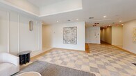 Located at 20-30 W Allens Lane in Philadelphia's Mt. Airy neighborhood, this thoughtfully designed lobby serves as the welcoming centerpiece of a modern residential building. The space is organized across a single floor and encompasses a vestibule, hallway, lounge areas, and a dedicated mailroom.

Entry is made through a striking glass-and-steel vestibule framed by floor-to-ceiling black-framed glazing, allowing natural light to pour in while offering views of the surrounding streetscape. A checkered stone tile floor anchors the transition zone, giving way to warm light hardwood flooring throughout the main lobby.

The lounge area is furnished with plush, neutral-toned armchairs and a sleek marble side table, positioned alongside expansive floor-to-ceiling windows that frame views of the neighborhood. Curated large-format abstract artwork adorns the crisp white walls, lending a gallery-like ambiance to the space. Recessed lighting and subtle wall sconces complement the natural light, creating a warm and polished atmosphere.

The mailroom features a clean, well-lit layout lined with rows of dark metal individual mailboxes, decorated with a single framed artwork on the wall. The hallway connects the various areas efficiently, maintaining the contemporary aesthetic throughout with consistent finishes and recessed ceiling lighting.