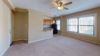 Located at 6104 S Woodlawn Ave in Chicago's Woodlawn neighborhood, this single-floor unit offers a practical and functional layout designed for comfortable living. The open living area is finished with plush carpeting and features a ceiling fan with light fixture, creating a bright and airy atmosphere. Large windows allow natural light to fill the space, with views of the surrounding neighborhood. The kitchen flows seamlessly from the living area via a half-wall breakfast bar, providing a convenient pass-through design. The kitchen itself is equipped with warm honey-toned wood cabinetry, ample counter space with a neutral laminate surface, a black gas range with oven, a double sink, and tile flooring that adds a clean, durable finish. Additional upper cabinetry and shelving provide generous storage. The bedroom is generously sized with soft carpet flooring, a ceiling fan, and two closets offering abundant storage — one of which is a walk-in. A classic cast-iron radiator provides supplemental heating. The full bathroom includes a bathtub and shower combo with white tile surround, a vanity with under-cabinet storage, a medicine cabinet mirror, and two windows that bring in natural light while maintaining privacy.