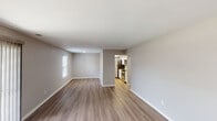 Located at 4227 Mission Dr in Indianapolis, Indiana, this single-story space offers a clean, modern aesthetic throughout. Consistent light wood-style flooring flows seamlessly across all rooms, complemented by neutral gray walls and crisp white trim, creating a cohesive and contemporary atmosphere.

The open living area is generously proportioned, featuring a sliding glass door fitted with vertical blinds that allows natural light to fill the space. This area connects fluidly to a second living or dining space, which opens directly into the kitchen through a defined passageway.

The kitchen is well-appointed with white shaker-style cabinetry, granite-look countertops, and a full suite of stainless steel appliances, including a refrigerator, electric range, built-in microwave, and dishwasher. Overhead lighting brightens the galley-style layout efficiently.

Multiple additional rooms provide flexible living options, each featuring windows with blinds that offer views of the surrounding neighborhood. Two bathrooms serve the space: one includes a walk-in shower with a white vanity, while the other features a full tub-shower combination, both finished with matching light flooring and neutral tones throughout.