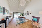 Located at 373 Western Dr in Santa Cruz, California, this single-floor amenity space is thoughtfully designed to maximize both function and aesthetic appeal. The architecture is defined by a dramatic vaulted ceiling with exposed white-painted beams and shiplap detailing, creating a sense of openness that exceeds what the floor area alone might suggest. A large sculptural woven globe pendant light serves as a striking focal point overhead.

The space is divided into two functional zones. A lounge area features a bold geometric patterned accent wall with modern egg-style chairs and a round artisan side table, providing a comfortable, inviting setting for casual gatherings. The opposite zone hosts a sleek marble-topped communal table with leather bar-height chairs, ideal for collaborative work or dining.

Light wood-look flooring runs throughout, anchored by a vibrant multi-toned area rug. A beverage and coffee station with under-counter refrigeration lines one wall, adding practical amenity value. A cluster of hexagonal wood-framed mirrors provides decorative depth.

Floor-to-ceiling sliding glass doors open toward an outdoor pool area, flooding the interior with natural light and offering seamless indoor-outdoor connectivity. High clerestory windows further enhance the bright, airy California ambiance.