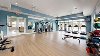 Located at 101 Grand Bahama Dr in Conway, South Carolina, this single-floor fitness center offers a well-appointed and expansive workout environment designed to accommodate a full range of exercise routines. The space is finished with light hardwood-style flooring throughout, complemented by soft blue-painted walls and crisp white trim that create a clean, energizing atmosphere. Ceiling fans are strategically placed to maintain comfortable airflow across the open floor plan.

The main workout area is generously sized and features a comprehensive selection of strength training machines, including multi-functional cable and weight equipment, as well as adjustable benches and a dumbbell rack. Cardio equipment such as treadmills, ellipticals, and stationary bikes are positioned near floor-to-ceiling windows that provide natural light and views of the outdoor surroundings, including what appears to be a pool area. Wall-mounted televisions are installed throughout for entertainment during workouts.

A dedicated studio space adjoins the main floor, equipped with cycling bikes, stability balls, and a large mirrored wall that enhances the sense of space and supports form-focused training. The studio also features a mounted display screen for guided fitness classes. Recessed lighting and multiple windows ensure the entire facility remains bright and inviting, making this fitness center a comprehensive and functional amenity.