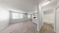 Located at 27 N 28th St in Las Vegas, NV, this single-floor unit offers a practical and well-organized layout. The open-concept living area features neutral gray walls, soft carpeting, and a textured ceiling, creating a clean and bright atmosphere. Windows along the living room wall allow natural light to filter in, enhancing the airy feel of the space. A wall-mounted air conditioning unit provides climate control directly in the living area.

The kitchen is semi-open to the living space, separated by a white peninsula counter that doubles as a breakfast bar. It is equipped with white cabinetry, a black electric range with a range hood, a black refrigerator, and a single-basin sink — offering all the essentials in a compact, efficient footprint. Wood-look vinyl flooring runs throughout the kitchen area, providing a clean contrast to the carpeted living space.

The bedroom is a quiet, carpeted retreat with access to an open closet with shelving, providing ample organizational space. The full bathroom features wood-look vinyl flooring, a white vanity, a toilet, and a tub-shower combination with white tile surround. Throughout the unit, the consistent light gray color palette and clean finishes give the space a modern, move-in-ready appearance.