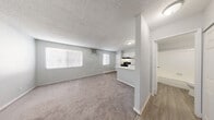Located at 27 N 28th St in Las Vegas, NV, this single-floor unit offers a practical and well-organized layout. The open-concept living area features neutral gray walls, soft carpeting, and a textured ceiling, creating a clean and bright atmosphere. Windows along the living room wall allow natural light to filter in, enhancing the airy feel of the space. A wall-mounted air conditioning unit provides climate control directly in the living area.

The kitchen is semi-open to the living space, separated by a white peninsula counter that doubles as a breakfast bar. It is equipped with white cabinetry, a black electric range with a range hood, a black refrigerator, and a single-basin sink — offering all the essentials in a compact, efficient footprint. Wood-look vinyl flooring runs throughout the kitchen area, providing a clean contrast to the carpeted living space.

The bedroom is a quiet, carpeted retreat with access to an open closet with shelving, providing ample organizational space. The full bathroom features wood-look vinyl flooring, a white vanity, a toilet, and a tub-shower combination with white tile surround. Throughout the unit, the consistent light gray color palette and clean finishes give the space a modern, move-in-ready appearance.