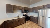 Located at 3700 42nd St S in Fargo, North Dakota, this single-floor unit offers a thoughtfully designed layout with modern finishes throughout. The kitchen is a standout feature, showcasing rich dark-stained cabinetry, light quartz countertops, and a full suite of stainless steel appliances including a refrigerator, electric range with over-the-range microwave, and dishwasher. A deep undermount sink with a matte black faucet adds a contemporary touch, while recessed lighting illuminates the space efficiently. Light wood-look flooring flows seamlessly throughout the entire unit, creating a cohesive and clean aesthetic. The living area is open and airy, benefiting from large windows and a sliding glass door that leads to a private balcony, allowing for abundant natural light and outdoor views. A wall-mounted TV bracket and baseboard heating are practical built-in features of the living space. The bathroom is well-appointed with a wide vanity topped with a speckled quartz countertop, an undermount sink, matte black fixtures, and a large mirror. A hallway connects the bathroom to an adjacent room with a bright window, enhancing the sense of openness. The overall ambiance is clean, contemporary, and move-in ready, reflecting quality craftsmanship in a convenient Fargo location.
