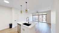 Located in the heart of Houston's Galleria area, this contemporary one-bedroom, one-bathroom residence on Post Oak Boulevard offers a well-designed layout with modern finishes throughout. Light wood-style flooring flows seamlessly across the entire unit, creating a warm and cohesive aesthetic.

The open-concept kitchen and living area serves as the heart of the home. The kitchen is outfitted with white shaker cabinetry, quartz countertops, a large center island with an undermount sink and industrial-style faucet, stainless steel appliances, and a textured tile backsplash. Stylish gold pendant lights add a sophisticated accent. The spacious living area features ceiling fans with lighting, recessed fixtures, and floor-to-ceiling sliding glass doors that open to a private balcony with metal mesh railings and views of the surrounding urban landscape.

The generously sized primary bedroom includes a ceiling fan, large windows for ample natural light, and access to a dedicated closet. The full bathroom is finished with a white vanity, quartz countertop, black-framed mirror, white cabinetry, and a tiled soaking tub and shower combination. Clean lines and a neutral palette create a calm, functional space throughout.