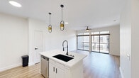 Located in the heart of Houston's Galleria area, this contemporary one-bedroom, one-bathroom residence on Post Oak Boulevard offers a well-designed layout with modern finishes throughout. Light wood-style flooring flows seamlessly across the entire unit, creating a warm and cohesive aesthetic.

The open-concept kitchen and living area serves as the heart of the home. The kitchen is outfitted with white shaker cabinetry, quartz countertops, a large center island with an undermount sink and industrial-style faucet, stainless steel appliances, and a textured tile backsplash. Stylish gold pendant lights add a sophisticated accent. The spacious living area features ceiling fans with lighting, recessed fixtures, and floor-to-ceiling sliding glass doors that open to a private balcony with metal mesh railings and views of the surrounding urban landscape.

The generously sized primary bedroom includes a ceiling fan, large windows for ample natural light, and access to a dedicated closet. The full bathroom is finished with a white vanity, quartz countertop, black-framed mirror, white cabinetry, and a tiled soaking tub and shower combination. Clean lines and a neutral palette create a calm, functional space throughout.