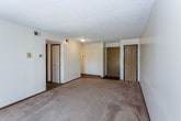 This single-floor unit offers a straightforward, functional layout across several interconnected rooms. The spacious living area features wall-to-wall carpet in a neutral beige tone, complemented by cream-colored walls and a textured ceiling. A sliding glass door leads to a private balcony, allowing natural light to fill the space. The living area connects openly to the kitchen, which is equipped with white cabinetry, light countertops, a double stainless steel sink, and a dishwasher, providing ample storage and prep space.

The bedroom is generously sized with carpeted flooring and features two separate closets with wood-paneled doors, offering plentiful storage. A window fitted with horizontal blinds brings in natural light. The bathroom is clean and functional, featuring a tub-shower combination, a toilet, and a single vanity with a light countertop and an overhead mirror with built-in lighting. Dark hardwood-style flooring adds contrast in the hallway and wet areas. Throughout the unit, dark baseboards provide a consistent visual accent against the light walls. The overall ambiance is neutral and move-in ready, offering a practical and comfortable living environment.
