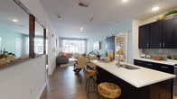 Located at 100 Town Center Blvd in Sewell, NJ, this single-floor residence offers a thoughtfully designed open-concept layout that seamlessly connects the kitchen, dining, and living areas. The kitchen is a standout feature, outfitted with rich dark shaker-style cabinetry, crisp white quartz countertops, a light grey subway tile backsplash, stainless steel appliances, and a central island with a built-in sink — ideal for both cooking and casual dining. The open living and dining area is anchored by warm hardwood-style flooring, light blue accent walls, and abundant natural light streaming through large windows. A stylish sliding barn door adds a distinctive architectural touch to the space. The living room provides a comfortable, generously sized area with easy access to natural light and views of the surrounding area. The primary bedroom features hardwood-style flooring, a large window with sheer curtains, and a soft green accent wall, creating a calm and restful atmosphere. The second bedroom is equally well-appointed with natural light and warm neutral tones. The bathroom is finished with white subway tile, a mosaic accent border, a soaking tub and shower combination, a dark-framed vanity mirror, and a crisp white countertop — delivering a clean, modern aesthetic throughout.