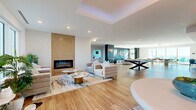 Located at 1216 N Atlantic Ave in Daytona Beach, Florida, this generously sized single-floor amenity space offers a thoughtfully designed, open-concept layout that seamlessly connects multiple functional zones. Throughout, warm-toned hardwood flooring and crisp white ceilings create a bright, modern aesthetic.

The main lounge area serves as the centerpiece, anchored by a floor-to-ceiling tile-clad linear fireplace and a striking tray ceiling with ambient lighting. Plush, neutral-toned sectional sofas and accent chairs are arranged around sculptural coffee tables, creating an inviting atmosphere for relaxation. Large windows allow abundant natural light to pour in, with views of the surrounding streetscape.

Adjacent to the lounge is a stylish wet bar featuring white subway tile backsplash, pendant lighting, and a long counter lined with teal velvet barstools — ideal for social gatherings. A billiards table anchors the game area nearby, complemented by bold teal accent walls and contemporary wall art.

A dedicated co-working area provides white work surfaces and teal swivel chairs, bathed in natural light from wide windows. A more intimate lounge nook, decorated with a navy slatted accent wall and coastal-inspired artwork, offers direct views toward the Atlantic Ocean. The space as a whole exudes a refined coastal-contemporary character suited for community living and entertainment.