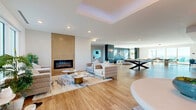 Located at 1216 N Atlantic Ave in Daytona Beach, Florida, this generously sized single-floor amenity space offers a thoughtfully designed, open-concept layout that seamlessly connects multiple functional zones. Throughout, warm-toned hardwood flooring and crisp white ceilings create a bright, modern aesthetic.

The main lounge area serves as the centerpiece, anchored by a floor-to-ceiling tile-clad linear fireplace and a striking tray ceiling with ambient lighting. Plush, neutral-toned sectional sofas and accent chairs are arranged around sculptural coffee tables, creating an inviting atmosphere for relaxation. Large windows allow abundant natural light to pour in, with views of the surrounding streetscape.

Adjacent to the lounge is a stylish wet bar featuring white subway tile backsplash, pendant lighting, and a long counter lined with teal velvet barstools — ideal for social gatherings. A billiards table anchors the game area nearby, complemented by bold teal accent walls and contemporary wall art.

A dedicated co-working area provides white work surfaces and teal swivel chairs, bathed in natural light from wide windows. A more intimate lounge nook, decorated with a navy slatted accent wall and coastal-inspired artwork, offers direct views toward the Atlantic Ocean. The space as a whole exudes a refined coastal-contemporary character suited for community living and entertainment.