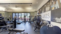 The Axis Fitness Center is a thoughtfully designed, single-level facility offering a comprehensive workout environment across several interconnected zones. The main exercise floor is generously proportioned, featuring durable speckled rubber flooring throughout and elevated ceilings with ceiling fans that promote airflow during intense workouts. Large floor-to-ceiling windows line one wall, flooding the space with natural light and providing views of lush outdoor greenery, creating an energizing atmosphere.

The cardio section is well-stocked with multiple treadmills and elliptical trainers positioned to take advantage of the outdoor views. Nearby, a robust selection of selectorized strength machines offers a full range of resistance training options, complemented by a dedicated free weights area housing a complete dumbbell rack and cable machine systems. Full-length mirrors along the walls enhance both the sense of space and functionality for form-checking during workouts.

A separate enclosed room, distinguished by vibrant teal accent walls, serves as a dedicated boxing and functional training area. It is equipped with speed bags, wall-mounted boxing equipment, and resistance training accessories. The facility also features dramatic large-scale athletic photography murals along the walls, reinforcing the space's energetic and motivating aesthetic throughout.