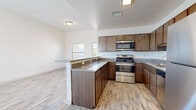 This three-story home is designed with a functional and straightforward layout that makes efficient use of space across all levels. The kitchen serves as a central highlight, featuring warm medium-toned wood cabinetry paired with granite countertops that extend across both the main cooking area and a peninsula breakfast bar. Stainless steel appliances, including an electric range and built-in microwave, provide a modern contrast to the classic cabinetry. Wood-look tile flooring runs throughout the kitchen and adjacent living area, adding visual warmth and durability. The living space adjoins the kitchen in an open-concept fashion, with a window allowing natural light and outdoor views.

Bedrooms are finished with plush carpet flooring and feature windows that bring in additional natural light. The bathroom is clean and bright, outfitted with a full soaking tub and tiled shower surround in crisp white. Throughout the home, white walls create a neutral backdrop that enhances the sense of light and openness. The attached garage offers generous space with a concrete floor and an automatic opener, providing practical convenience. The exterior 3D scan reveals dual HVAC units and mature landscaping surrounding the structure.