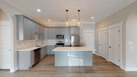 Located at 1230 Cottontown Rd in Forest, VA, this single-floor home offers a thoughtfully designed layout with modern finishes throughout. The kitchen is a standout feature, showcasing grey shaker-style cabinetry, white quartz countertops, a subway tile backsplash, and a full suite of stainless steel appliances including a range, microwave, dishwasher, and refrigerator. A central island with a bright white finish and pendant lighting above adds both functionality and visual appeal. Light wood-look flooring runs through the main living and kitchen areas, complementing the neutral color palette. The living space features crown molding, recessed lighting, a ceiling fan, and an elegant arched double-door entry that invites natural light into the room. Bedrooms are finished with plush carpet, ceiling fans, and large windows with blinds that allow for ample natural light. The bathrooms are well-appointed with grey vanities, white quartz countertops, tub-shower combos, and diagonal-set tile flooring. A light-filled hallway with wood-look flooring connects the rooms seamlessly. The home's cohesive design, combining contemporary finishes with functional spaces, creates a comfortable and inviting living environment.