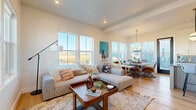 Located at 1502 Victoria St in Bozeman, Montana, this well-appointed two-story home offers three bedrooms and three bathrooms across two floors of thoughtfully designed living space. The main floor welcomes you through a bold black entry door into an open-concept layout where the living room, kitchen, and dining area flow seamlessly together over light hardwood flooring. The kitchen is a standout, featuring crisp white shaker cabinetry with matte black hardware, grey subway tile backsplash, stainless steel appliances, a statement range hood, and a generous island with bar seating. The adjacent dining area is bathed in natural light from large wraparound windows that frame sweeping views of the surrounding Montana landscape, anchored by a striking mixed-metal chandelier. Upstairs, the primary bedroom offers a comfortable retreat with plush carpeting and bright windows. The primary bathroom impresses with a double-sink vanity, warm wood cabinetry, dark countertops, and a sleek frameless glass shower clad in marble-style tile. Additional bathrooms echo the same refined aesthetic with wood-toned vanities, dark countertops, and marble-tiled tub-shower combinations. Throughout the home, a cohesive palette of warm neutrals, natural wood tones, and modern fixtures creates an inviting yet polished atmosphere.