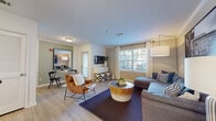 Located in Groton, Connecticut, this single-floor residence offers a thoughtfully designed layout with a comfortable and contemporary aesthetic throughout. The open-concept living area serves as the heart of the home, featuring light wood-style flooring, crown molding, and generous natural light streaming through large windows dressed with floor-length curtains. A versatile seating arrangement anchors the space, with direct sightlines to a dedicated dining nook and the kitchen beyond.

The kitchen is well-equipped with stainless steel appliances — including a gas range, built-in microwave, and full-size refrigerator — complemented by crisp white cabinetry, dark countertops, and a breakfast bar with seating. Ample storage and prep space make this kitchen both functional and visually clean.

The bedroom is a serene retreat, highlighted by a muted blue accent wall, plush carpeting, and a spacious walk-in closet with wire shelving and dual hanging rods. Natural light filters in through curtained windows, enhancing the calm atmosphere of the room.

The full bathroom features a white vanity with a broad mirror, a combination tub and shower, and wood-look tile flooring, offering a clean and classic finish. Additional cabinetry near the kitchen entry provides convenient extra storage. The overall design balances practicality with a welcoming, modern sensibility.