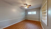 This single-floor home offers a cohesive and practical layout designed for comfortable everyday living. Throughout the space, warm-toned hardwood-style flooring creates a consistent and inviting aesthetic, complemented by soft gray walls and crisp white baseboards that lend a clean, modern feel to every room.

Each room is equipped with a ceiling fan with integrated lighting, providing both comfort and illumination. The rooms are well-lit by natural light streaming through windows fitted with horizontal blinds, offering privacy while maintaining brightness. Several rooms also feature wall-mounted air conditioning units for added climate control.

The kitchen stands out with its white shaker-style cabinetry, light countertops, and a striking blue elongated subway tile backsplash. Stainless steel appliances, including an electric range and over-the-range microwave, complete the functional and stylish cooking space.

The bathroom features a full tub-shower combination finished with classic white subway tiles, accented by a decorative mosaic border. Brass-toned fixtures add a warm, timeless touch, while a small window above the tub allows for natural ventilation and light.

The floor plan, as seen in the dollhouse view, reveals a compact yet efficiently organized layout with clearly defined living areas, bedroom spaces, and utility zones — making this home a well-rounded and move-in ready space.