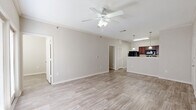 This thoughtfully designed single-floor residence offers a comfortable and functional layout across a well-utilized footprint. Light-toned wood-look flooring runs throughout the main living areas, creating a clean and cohesive aesthetic, while neutral warm-gray walls provide a versatile backdrop throughout.

The open-concept living room is bright and airy, featuring crown molding, a ceiling fan with light fixture, and a set of French doors that lead to a private balcony, allowing natural light to fill the space. The kitchen is positioned adjacent to the living area and features rich dark-wood cabinetry, light stone-look countertops, a peninsula breakfast bar with pendant lighting, and a full suite of black appliances including a refrigerator, electric range, and microwave.

The bedroom offers a comfortable, carpeted retreat with its own ceiling fan and a window providing natural light. A dedicated office space adds flexibility for remote work or study. The full bathroom includes a dark-wood vanity with a stone-look countertop, a full soaking tub and shower combination, and matching wood-look flooring. Additional conveniences include a hallway, a closet for storage, and an in-unit laundry area, making this residence both practical and inviting.