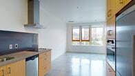 This single-floor unit showcases a distinctly modern design aesthetic, anchored by polished concrete floors that run seamlessly throughout the entire space, reflecting natural light and lending an industrial-chic quality to every room. Crisp white walls and clean lines create a bright, minimalist atmosphere that feels open and uncluttered.

The kitchen is thoughtfully appointed with warm bamboo cabinetry, concrete countertops, a stainless steel sink, a gas cooktop, a stainless steel range hood, a built-in dishwasher, and a dark metal backsplash that adds contrast to the natural wood tones. Open upper shelving provides additional storage and display space.

The main living area is generously proportioned, bathed in natural light from a bank of wood-framed windows that frame views of the surrounding urban skyline and greenery. A wall-mounted mini-split HVAC unit ensures year-round climate comfort. The open layout between the kitchen and living area encourages a flexible, functional arrangement.

The bathroom features subway tile surrounding a soaking tub with an overhead shower, a concrete-topped vanity with an undermount sink, and warm wood cabinetry below, maintaining the cohesive material palette found throughout the unit. Overall, the space offers a refined, contemporary urban environment with durable, high-quality finishes.