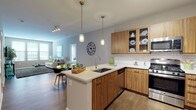 This single-floor residence offers a thoughtfully designed open-concept layout that seamlessly connects the kitchen, dining, and living areas. The kitchen is a standout feature, equipped with warm wood cabinetry, a classic subway tile backsplash, stainless steel appliances, and a large peninsula with a built-in sink and white quartz countertop that doubles as a breakfast bar with seating. Pendant lighting above the peninsula adds a modern, polished touch. The living room is bright and welcoming, featuring hardwood-style flooring, neutral walls, and multiple windows that invite natural light. The bedrooms are carpeted and generously sized, offering a comfortable retreat. One bedroom includes access to a spacious walk-in closet outfitted with wire shelving systems for organized storage. The residence includes two full bathrooms, each finished with tile flooring and wood-toned vanities with white countertops. One bathroom features a combined tub and shower, while the other offers built-in wall shelving for additional storage. Throughout the space, a consistent neutral color palette and clean finishes create a cohesive, modern ambiance suited for everyday living.