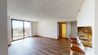 This single-floor residence offers a thoughtfully designed layout that balances open communal spaces with comfortable private quarters. The living area is spacious and bright, anchored by wood-look plank flooring and large floor-to-ceiling sliding glass doors that open to a private balcony, flooding the room with natural light and framing sweeping views of the surrounding cityscape and greenery.

The kitchen is efficiently organized in a galley-style configuration, featuring warm honey-toned wood cabinetry, granite countertops, a decorative mosaic tile backsplash, and black appliances. A peninsula with bar seating for three connects the kitchen to the main living area, creating a seamless space ideal for casual dining or entertaining.

The bedrooms are carpeted for comfort and include generous closet space with built-in shelving. Each room benefits from windows that continue the residence's theme of natural light and elevated views. The primary bathroom includes a double-sink vanity with granite countertops, warm wood cabinetry, and tile flooring, while the second bathroom features a clean, white tub-shower combination with tile flooring. Throughout the unit, warm wood trim and neutral tones create a cohesive, welcoming ambiance.