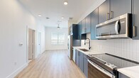 Located at 3939 W 12th St in Houston, TX, this efficient one-bedroom, one-bathroom unit offers a thoughtfully designed single-floor layout. The open-concept kitchen and living area is anchored by a striking kitchen featuring floor-to-ceiling blue-grey cabinetry with gold-toned hardware, white quartz countertops, a white subway tile backsplash, and a full suite of stainless steel appliances including a French door refrigerator, electric range, built-in microwave, and dishwasher. A matte black gooseneck faucet adds a refined finishing touch. Light wood-tone flooring extends throughout the main living area, complemented by recessed lighting and a ceiling fan that enhance both illumination and airflow. A window in the living area invites natural light into the space. The bedroom features neutral carpet flooring, crisp white walls, and a closet with a built-in rod for ample storage. The bathroom is a design standout, clad in dramatic marble-look tile from floor to ceiling surrounding a soaking tub and shower combination, with matte black fixtures providing a bold contrast to the white surfaces. The overall aesthetic is clean, contemporary, and well-appointed throughout.