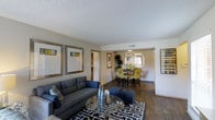 Located in Euless, TX, this single-story residence offers an open-concept layout that seamlessly connects the living and dining areas, creating a cohesive and functional flow throughout the main living space. The living area is anchored by hardwood-style flooring that extends into the dining space, providing a warm and consistent aesthetic underfoot. Neutral-toned walls serve as a versatile backdrop, complementing a variety of décor styles. A textured ceiling adds subtle architectural character to the interior. The living room offers ample space for comfortable seating arrangements, as seen with a generous sofa, ottoman, and glass-top coffee table. Framed wall art and a bold geometric area rug contribute to a polished, contemporary feel. Transitioning into the dining area, the space accommodates a full dining set with seating for multiple guests, highlighted by natural light filtering in through a window. A decorative indoor plant adds a touch of greenery to the dining zone. The overall ambiance is bright, welcoming, and well-appointed, making it a comfortable and practical living environment.