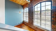 This two-story unit at 1101 Hawthorne Lane blends industrial character with modern finishes. The main floor showcases dramatic arched windows set in exposed brick walls, warm wood-plank ceilings, and rich hardwood floors, all bathed in abundant natural light. The open kitchen features granite countertops, dark wood cabinetry, stainless steel appliances, and a large island with a built-in sink. Upstairs, the bedrooms offer wood ceilings, hardwood or light wood flooring, and generous closet space with sliding doors. Both bathrooms are finished with granite vanities and clean, bright fixtures. A staircase connects the two well-proportioned floors, creating a loft-like, open ambiance throughout.
