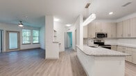 This single-floor residence is designed with a clean, contemporary aesthetic that emphasizes open living. The kitchen is a standout feature, equipped with stainless steel appliances including a side-by-side refrigerator, electric range, and built-in microwave. Light wood-toned cabinetry lines the walls from floor to ceiling, complemented by granite countertops and a subway tile backsplash. A peninsula with a built-in sink and matching granite surface serves as both a functional workspace and a natural divider between the kitchen and the main living area, which is illuminated by a modern pendant light fixture.

The open living and dining area is bright and spacious, featuring wood-look plank flooring, white walls, and a ceiling fan. Natural light enters through multiple windows, offering views of surrounding greenery. Built-in shelving adds a practical architectural detail near the entryway.

The bedrooms feature plush carpet, ceiling fans, and natural light from windows with blinds. One bedroom provides direct access to a closet and bathroom.

Two bathrooms offer refined finishes, including granite-topped vanities, wood-toned cabinetry, and large-format stone-tiled surrounds. One bathroom features a soaking tub with a sliding glass enclosure, while the other includes a dedicated walk-in shower, creating distinct and functional bathing spaces.