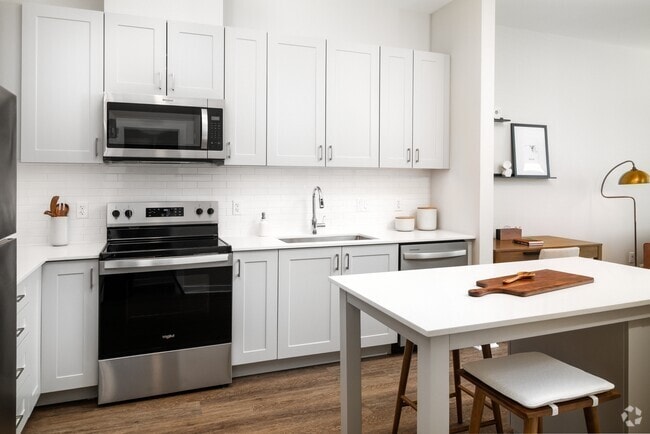 New West Phase - Finish Package III Kitchen with stainless steel appliances, white quartz countertops, grey cabinetry, pendant lighting, and hard surface flooring - Avalon Hunt Valley and Hunt Valley West