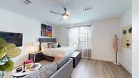 Located at 72 Milton Ave SE in Atlanta, GA, this single-floor unit offers a thoughtfully designed layout with modern finishes and a bright, contemporary aesthetic throughout. The galley-style kitchen is a standout feature, equipped with stainless steel appliances including an electric range, microwave, and dishwasher. Crisp white cabinetry pairs elegantly with gray quartz countertops and a striking blue tile backsplash, while light wood-look flooring runs seamlessly throughout the space. The bedroom is generously proportioned, offering room for a full sitting area alongside the bed, and is complemented by a ceiling fan, natural light from a large window with sheer curtains, and a walk-in closet accessible via a sliding door. The living area flows naturally from the bedroom, creating an open, flexible space well-suited to a variety of arrangements. A wall-mounted flat-screen television and a round decorative mirror add functional style to the living zone. The bathroom features a full soaking tub with shower combination, set against clean white tile and warm wood-look flooring. Throughout the unit, recessed lighting, white walls, and an airy open feel contribute to a cohesive, modern ambiance that is both inviting and functional.
