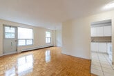 This three-bedroom, two-bathroom unit at 1875 Steeles Ave W in Toronto offers a practical and well-laid-out single-floor living space. The open living and dining area is highlighted by warm parquet hardwood flooring that runs throughout the main living spaces, with large windows that invite natural light and offer pleasant outdoor views. The kitchen is efficiently designed with white cabinetry extending to the ceiling for ample storage, a tile backsplash, white appliances including a refrigerator and electric range, and durable tile flooring. The primary bedroom is generously sized and features sliding closet doors, while the two additional bedrooms also feature the same warm parquet flooring and built-in storage. The main bathroom includes a vanity with an under-sink cabinet, a wall-mounted mirror, tile surround, and a bathtub. A secondary bathroom provides a toilet and window for natural ventilation. A hallway connects the bedrooms to the main living areas, providing a clear and functional flow throughout the unit. Baseboard heating is present throughout, ensuring year-round comfort in this well-structured Toronto residence.