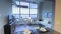 Located at 201 S 25th Street in Philadelphia's desirable Rittenhouse Square neighborhood, this single-floor loft showcases a striking industrial-chic aesthetic that seamlessly blends raw architectural character with modern living. The space is defined by its dramatic floor-to-ceiling factory-style windows, which span nearly an entire wall and flood the interior with abundant natural light while offering sweeping views of the surrounding cityscape.

The open-concept layout allows the living, dining, and kitchen areas to flow naturally into one another, creating a spacious and versatile environment. Soaring ceilings with exposed ductwork and industrial fixtures reinforce the building's converted warehouse heritage, lending the space an authentic urban character. Original brick detailing adds warmth and texture to the walls, complementing the polished concrete flooring throughout.

The living area is generously proportioned, comfortably accommodating a large sectional seating arrangement, while the adjacent dining space is well-suited for entertaining. Ceiling fans provide practical comfort beneath the lofty overhead expanse. The combination of expansive glazing, high ceilings, and thoughtfully curated finishes creates an ambiance that is both airy and sophisticated — a compelling example of Philadelphia's industrial architectural heritage reimagined for contemporary urban living.