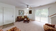 This two-story residence in Savannah, Georgia offers a thoughtfully arranged layout designed for comfortable everyday living. The main level features a bright living room with plush carpeting, a ceiling fan, and sliding glass doors that open to outdoor greenery, filling the space with natural light. Adjacent to the living area is a cozy dining nook illuminated by a stylish chandelier and framed by a window with floor-length drapes, creating an inviting atmosphere for meals. The kitchen is efficiently designed with white cabinetry, light countertops, and a full suite of appliances including a coil-top range with an over-the-range microwave, offering ample storage and workspace. A full bathroom on the main level features a tub-shower combination, a white vanity with under-sink storage, and a well-placed mirror. The upper level hosts the bedroom, a serene retreat with angled ceilings that add architectural character, soft carpet underfoot, and generous wall space. A full bathroom accompanies the bedroom, completing the private quarters. Throughout the home, neutral tones and clean finishes create a calm, cohesive aesthetic, while the multi-level design adds a sense of dimension and functionality to this Savannah address.