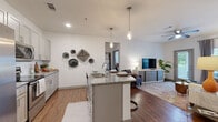 This single-floor residence offers a thoughtfully designed open-concept layout that seamlessly connects the kitchen, dining, and living areas. The kitchen is a standout feature, equipped with gray shaker-style cabinetry, granite countertops, stainless steel appliances, a white subway tile backsplash, and a central island with a double sink and pendant lighting overhead — ideal for both cooking and casual dining. Wood-style flooring runs throughout the main living areas, adding warmth and continuity to the space.

The living room is bright and welcoming, with large windows and a glass door providing ample natural light and outdoor views, complemented by a ceiling fan for added comfort. Two well-proportioned bedrooms each feature plush carpeting, large windows that let in natural light, and ceiling fans. Both bedrooms are paired with private bathrooms finished with granite-top vanities, gray cabinetry, wood-style flooring, and access to walk-in closets with built-in shelving and hanging rods. The clean, neutral color palette throughout the residence creates a cohesive and modern aesthetic, while the open floor plan ensures a comfortable flow between all living spaces.