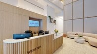 Located at 229 Duffield Street in the heart of Downtown Brooklyn, this thoughtfully designed lobby and common area serves as the welcoming face of Webster Apartments. The space spans a single floor and is organized into a reception area, a living room lounge, a library, a hallway, and an accessible bathroom.

The reception area is anchored by a sculptural, fluted wood desk finished in warm natural tones, branded with the Webster name. Behind the desk, a built-in wood panel wall features an embedded display screen, open shelving with trailing greenery, and integrated workstations. The floor-to-ceiling glass storefront along the entrance fills the space with abundant natural light and offers open views of Duffield Street, creating a bright and transparent connection to the surrounding neighborhood.

Soaring ceiling heights define the main lounge area, which is further accentuated by large, grid-patterned wall panels in muted neutral tones with warm gold trim. Polished marble-look flooring flows throughout, enhancing the sense of openness and elegance. Curved, cream-colored sofas and rounded accent chairs are arranged around low tables, creating an inviting and comfortable seating area.

The accessible bathroom is clean and functional, finished entirely in white tile with stainless steel grab bars and modern fixtures, meeting accessibility standards. The overall ambiance of the space is modern, airy, and welcoming, with a cohesive warm-neutral palette throughout.