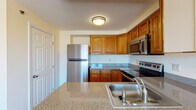 Located at 600 Bennett Way in Newmarket, New Hampshire, this single-floor residence offers a well-organized layout designed for comfortable everyday living. The kitchen is a functional centerpiece, featuring warm honey-toned wood cabinetry, granite-style countertops, and a breakfast bar peninsula that opens to the adjacent living area. Stainless steel appliances — including a refrigerator, electric range, and over-the-range microwave — complete the space, which also features hardwood flooring for a clean, polished look. The living area continues the hardwood flooring and is bathed in natural light, with a sliding glass door providing direct access to a private balcony that overlooks the surrounding neighborhood. The bedrooms are carpeted and finished with neutral tones, offering a calm and restful atmosphere. Each bedroom benefits from natural light through double-hung windows, with baseboard heating units lining the walls for year-round comfort. The bathroom includes a full soaking tub and shower combination with clean white surround. Throughout the residence, the warm cream-colored walls, white trim, and consistent finishes create a cohesive and inviting ambiance well-suited to a variety of lifestyles.
