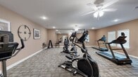 Located at 3825 Jonesboro Rd in South Fulton, GA, this fitness center offers a well-organized and functional workout space designed to support a range of cardio-focused exercise routines. The room is finished with warm beige walls and durable patterned carpet flooring, creating a clean and welcoming atmosphere throughout.

The space is equipped with a variety of cardio machines, including treadmills, elliptical trainers, a recumbent bike, and an upright stationary bike, providing users with diverse options for their fitness needs. A freestanding dumbbell rack adds a strength training element to the room's offerings. A full-length wall mirror spans one side of the room, effectively amplifying the sense of space and allowing users to monitor their form during workouts.

Recessed lighting and multiple ceiling fans with integrated light fixtures provide consistent illumination and airflow throughout the room, ensuring a comfortable environment during exercise. A wall-mounted flat-screen television is positioned for easy viewing from the equipment area. Framed artwork and decorative wall accents add a finishing touch, elevating the space beyond a purely utilitarian setting. A windowed wall allows natural light to filter in, further brightening the interior. The fitness center is accessible via a keyed entry door, ensuring a secure and private environment for residents.