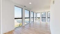 Located at 233 Lake Ave in Racine, Wisconsin, this modern 2-bedroom, 2-bathroom residence offers a thoughtfully designed single-level layout filled with natural light and impressive water views. The open-concept living room is a true highlight, lined with expansive floor-to-ceiling windows that frame sweeping panoramas of the marina and Lake Michigan, flooding the space with sunlight across light-toned hardwood flooring. The kitchen features a large quartz-topped island with an undermount sink, white shaker cabinetry, stainless steel appliances including a refrigerator, range, and microwave, and elegant pendant lighting overhead. Both bedrooms are carpeted for comfort and equipped with sliding barn-style doors and ceiling fans; the secondary bedroom enjoys its own window with views of the neighboring architecture. The two bathrooms are finished in a clean, contemporary style with wood-look flooring, white vanities with quartz countertops, and chrome fixtures — one featuring a full bathtub and shower combination. A dedicated in-unit laundry room with a Whirlpool washer and dryer and overhead wire shelving adds everyday convenience. Two closets and a bright, airy hallway complete this well-appointed residence.