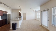 This single-story residence is designed with an open-concept layout that seamlessly connects the kitchen and living areas, creating a cohesive and functional living environment. The kitchen is outfitted with rich dark wood cabinetry, granite countertops, and stainless steel appliances, including a range, microwave, and refrigerator. A built-in wine rack adds a distinctive touch, while wood-style flooring grounds the space with warmth and durability. A peninsula with pendant lighting and a sink bridges the kitchen and the expansive living area, which transitions to plush wall-to-wall carpeting.

The living area is generously proportioned, featuring a ceiling fan with light kit, multiple windows dressed with blinds, and access to an exterior door that allows natural light to filter through. The bedrooms continue the carpeted flooring theme, each equipped with ceiling fans and ample natural light from windows with blinds. At least one bedroom features a walk-in closet with built-in shelving and hanging rods for organized storage.

The bathroom includes a double-sink vanity with dark wood cabinetry, a large mirror, and a full tub-shower combination with white tile surround. Overall, the space presents a clean, neutral palette throughout.