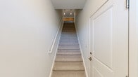 This two-story residence offers a thoughtfully designed layout across two levels, with the main living areas situated on the upper floor and additional space below. The open-concept kitchen and living room on the upper level serves as the heart of the home, featuring warm wood-toned cabinetry, stainless steel appliances including a refrigerator, microwave, and range, a white subway tile backsplash, dark countertops, and a large central island with pendant lighting overhead. Hardwood-style flooring flows throughout the main living areas, complemented by an abundance of natural light streaming through a sliding glass door that opens to an outdoor balcony. The four bedrooms are carpeted and bright, with white panel doors and generous closet space, including walk-in closets fitted with wire shelving systems. The two bathrooms are clean and modern, featuring wood-toned vanities, neutral countertops, and full tub-shower combinations with hardwood-style flooring. A dedicated laundry room houses a full-size Whirlpool washer and dryer. Carpeted stairs with a white handrail connect the two levels, accented by pendant lighting at the top landing. The overall aesthetic is clean, modern, and neutral throughout.