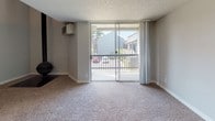 This two-floor residence offers a practical and comfortable layout with consistent finishes throughout. The living area is generously sized, featuring neutral-toned carpet, a textured ceiling, and a wall-mounted climate control unit. A sliding glass door opens directly to a private balcony, flooding the space with natural light and providing views of the surrounding neighborhood. The kitchen is well-appointed with white cabinetry, light countertops, and a full suite of black appliances including a refrigerator, range, dishwasher, and built-in range hood, all set atop durable wood-look flooring. Natural light enters through a slatted window blind, keeping the space bright and functional. The two bathrooms mirror each other in design, each featuring a soaking tub with white tile surround, a wide vanity with a light laminate countertop, a large mirror, and wood-look flooring with a baseboard heater. The bedrooms are carpeted and finished in soft neutral tones, with one featuring a sliding closet and another benefiting from large windows that bring in ample daylight. Clean white baseboards and a consistent gray-beige color palette create a cohesive, move-in-ready aesthetic throughout the home.
