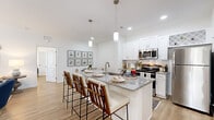 This single-floor residence offers a thoughtfully arranged layout encompassing two bedrooms, two bathrooms, a combined living and dining area, a full kitchen, and a hallway — all finished with consistent light-toned luxury vinyl plank flooring that runs throughout the space.

The open-concept kitchen, dining, and living area forms the heart of the unit. The kitchen is outfitted with white shaker cabinetry, granite countertops, a subway tile backsplash, stainless steel appliances, and a large island with bar seating illuminated by pendant lighting. Adjacent to the kitchen, the dedicated dining nook provides a defined space for a small dining set. The living room receives natural light through glass French doors and features a ceiling fan overhead.

The entry hallway offers a welcoming transition into the main living spaces. Both bedrooms are bright and comfortable, each featuring windows with natural views, light walls, and the same wood-look flooring. The primary bedroom provides a generous footprint. The two bathrooms include white vanity cabinetry with granite countertops and a tub-shower combination, maintaining the clean, cohesive aesthetic found throughout the unit.