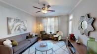 Located at Hurstbourne Estates, this single-story residence offers a cohesive and functional layout across several well-appointed rooms. The living area serves as the heart of the home, featuring crown molding, a ceiling fan, and large windows dressed with decorative gold-patterned curtains and plantation shutters that allow abundant natural light. The room accommodates a comfortable seating arrangement centered around a glass-top coffee table atop a plush area rug, creating an inviting atmosphere.

The kitchen is outfitted with rich dark cabinetry extending to the upper walls, granite countertops, black appliances including an electric range and built-in microwave, and durable wood-look flooring. A kitchen island with a stainless steel sink adds additional prep space and functionality.

The bedrooms are carpeted for comfort and each includes a ceiling fan and generous windows that bring in natural light. The primary bedroom features ample room for a full furniture suite, with direct access to a private bathroom equipped with a wide vanity, dual sinks, white countertops, dark cabinetry, and a shower-tub combination. A dedicated laundry room with full-size washer and dryer hookups adds notable convenience to the overall layout.