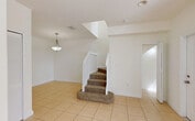Located at 1140 SE 24th Rd in Homestead, FL, this two-story home offers five bedrooms and three bathrooms spread across two thoughtfully laid-out floors. The ground floor features a kitchen equipped with rich cherry-toned cabinetry, granite-style countertops, a breakfast bar peninsula, white appliances, and track lighting — complemented by a pantry for additional storage. The adjacent living area is finished with light ceramic tile flooring, a ceiling fan, and a sliding glass door that brings in natural light and outdoor views. Carpeted stairs with white railings lead to the upper level, where the bedrooms are finished with light hardwood-style flooring and neutral walls. The primary bedroom includes a walk-in closet with wire shelving. Additional bedrooms feature built-in closets and windows with views of the surrounding greenery. The three bathrooms are finished with tile flooring and tub-shower combinations with tiled surrounds. A dedicated laundry room and utility space add everyday convenience. The exterior is surrounded by mature trees, offering a shaded, private setting in a residential Homestead neighborhood.
