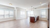 This efficiently designed one-bedroom unit offers a thoughtful layout across a single floor, making excellent use of its compact footprint. The open-concept living and dining area is bathed in natural light, courtesy of large sliding glass doors that lead to a private balcony overlooking the surrounding building exterior. Light hardwood-style flooring runs throughout the main living spaces, lending a warm, cohesive feel.

The kitchen is a standout feature, showcasing rich cherry wood cabinetry, granite countertops, and a full suite of stainless steel appliances, including a refrigerator, range, microwave, and dishwasher. A central island with a matching granite top provides additional prep space and casual dining potential.

The hallway connects the living area to the bedroom, and is distinguished by a striking sliding barn door in a deep mahogany finish, adding a modern, stylish touch. A traditional paneled door off the hallway provides access to additional storage or a closet.

The bedroom offers a quiet, cozy retreat with neutral-toned carpet flooring and clean white walls, creating a calm and restful atmosphere. Throughout the unit, a consistent neutral color palette, clean lines, and recessed lighting contribute to a bright, modern ambiance that is both functional and inviting.