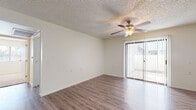 This single-floor unit offers a clean, functional layout spread across several distinct spaces. The living area is bright and open, finished with wood-look laminate flooring that extends throughout the main areas of the home. A ceiling fan with a light fixture is centrally positioned beneath a textured ceiling, providing both ventilation and ambient lighting. A sliding glass door fitted with vertical blinds opens to an outdoor space, allowing natural light to fill the room.

The kitchen is well-appointed with white cabinetry offering ample storage above and below the countertops. Dark laminate counters complement the suite of black and stainless steel appliances, which includes a gas range, over-the-range microwave, refrigerator, and dishwasher. A window above the sink introduces additional natural light into the space.

The bedroom is generously sized, with the same wood-look flooring continuing from the main living area. Natural light enters through a window, and a closet provides convenient storage. The bathroom features white tile walls surrounding a walk-in style shower area, with mosaic tile flooring and standard fixtures completing the utilitarian design. Overall, the unit presents a straightforward, well-maintained interior.