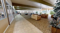 Located at 1177 Cardenas Dr SE in Albuquerque, New Mexico, this generously sized single-floor community space offers a versatile, open layout designed for recreation and socializing. The room is defined by its striking exposed wooden beams that run the length of the vaulted ceiling, complemented by white-paneled ceiling sections that lend a clean, airy aesthetic throughout.

The space is divided into several functional zones that flow seamlessly into one another. A recreation area houses two full-size pool tables, each illuminated by pendant lighting overhead, creating a focused yet comfortable atmosphere for gameplay. Adjacent to this area, multiple bistro-style tables with wrought iron chairs provide casual seating for dining or conversation. A lounge area features plush, earth-toned sofas and armchairs arranged around a wall-mounted television, offering a relaxed setting for gathering.

Large floor-to-ceiling windows line one side of the room, flooding the interior with natural light and providing views of the surrounding outdoor greenery. Potted plants are thoughtfully placed throughout, adding warmth and a natural touch. The flooring transitions between large-format tile along the perimeter and patterned carpet in the central areas, clearly delineating zones while maintaining visual cohesion. Overall, the space presents a welcoming and well-appointed environment suited for community activities.